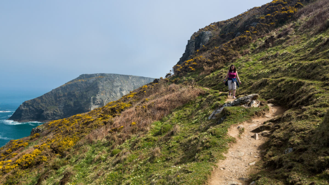Walker on a coastal path overlooking cliffs and sea near Tintagel in Cornwall