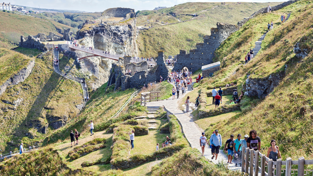 Visitors walking through the ruins of Tintagel Castle and crossing the historic bridge