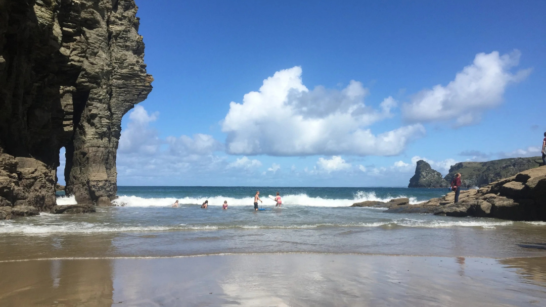 People enjoying Atlantic waves on a sandy beach near Tintagel with rocky cliffs